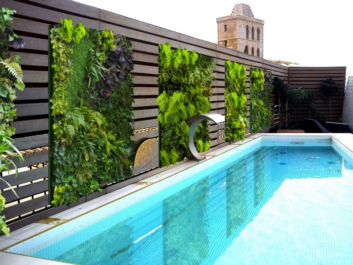 une piscine de luxe avec des murs végétaux installés sur la palissade en bois façon qui agissent comme un brise vue vegetal tout en créant une ambiance propice à la détente