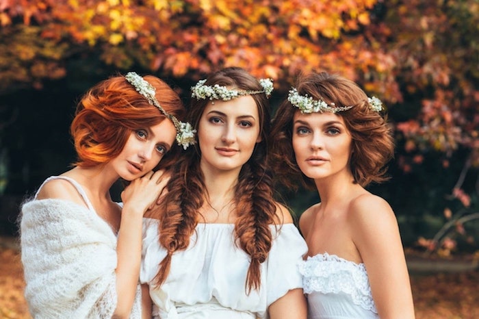 robe-de-mariée-blanche-boheme-chic-au-centre-entre-deux-femmes-une-femme-avec-deux-tresses-en-épi-et-couronne-de-fleurs-blanches-mariage-automne idée de coiffure mariage avec nattes en épi de coté, couronne de fleurs blanches, robes de mariées simples