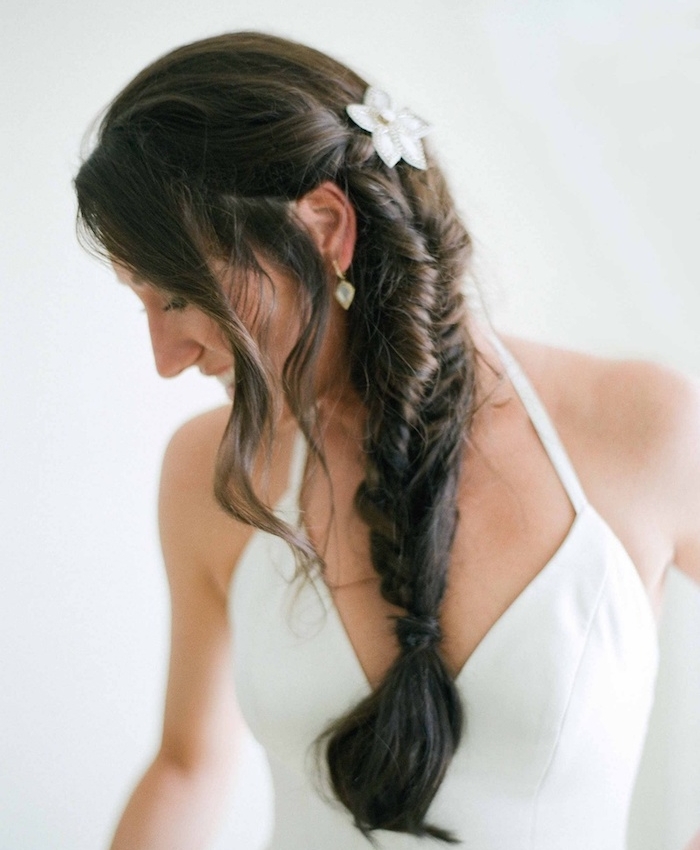 tresse mariée sur cheveux chatain foncé, mèches libres et une décoration de fleurs blanche, robe de mariée simple