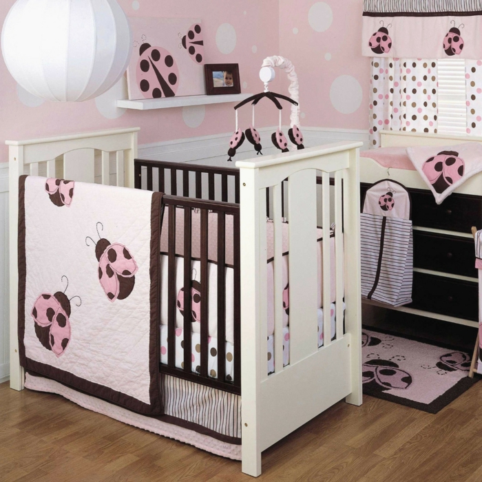 une chambre rose poudré, peinture rose poudré, couleur rose pale pour le linge de lit de bébé, motifs coccinelles, luminaire en forme de grande boule blanche en tissu blanc, petit tapis en rose et noir aux motifs coccinelles 