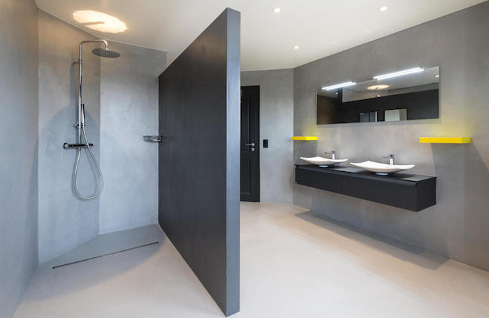 mur de sdb en béton ciré gris clair avec paroi separation de salle de bain sur sol cimenté