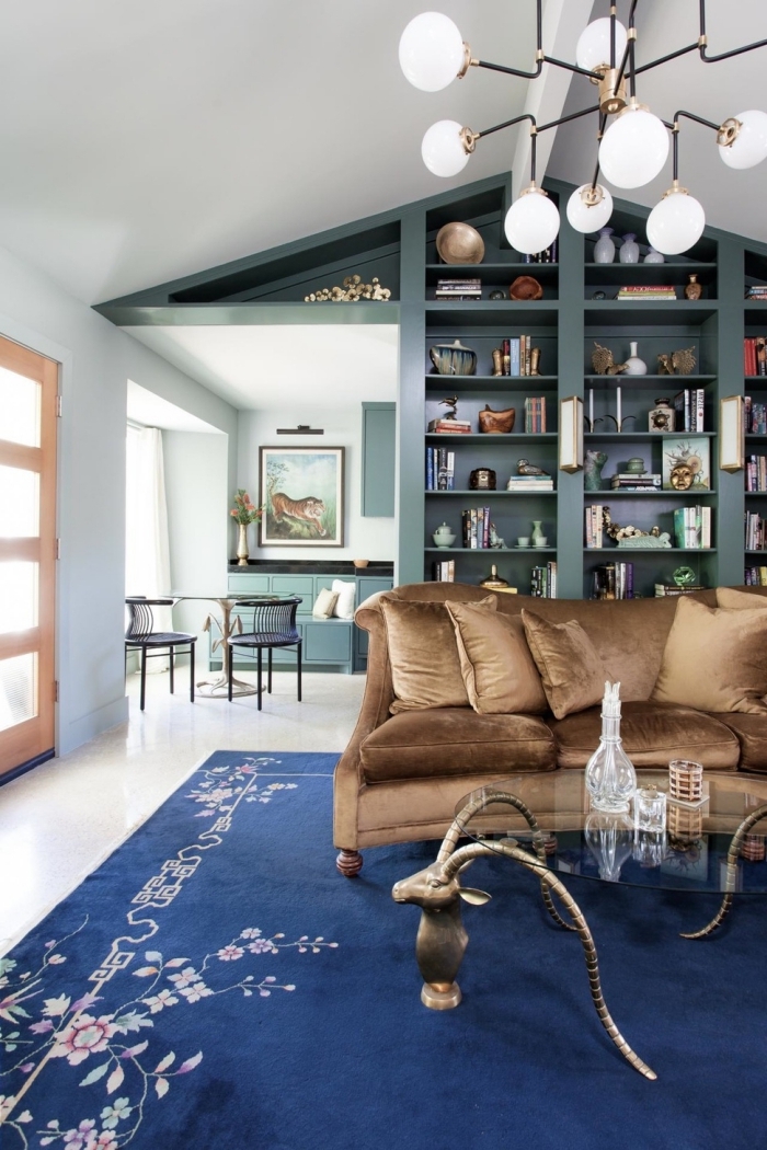 idée pour une deco bleu canard dans le salon, un mur bibliothèque couleur bleu canard aux petites touches de laiton qui s'harmonise avec le canapé en velours marron 