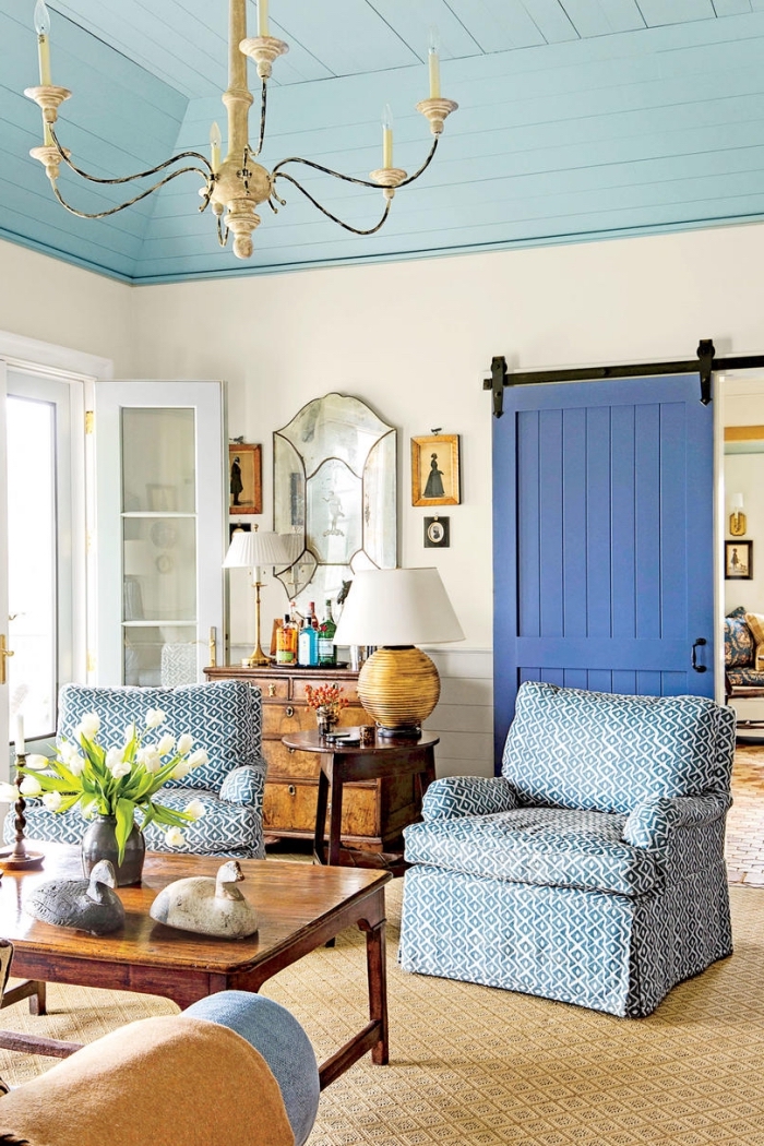 une porte de grange coulissante peinte en bleu avec une poignée et des rails contrastants en noir qui s'harmonise avec la déco de charme du salon campagne chic