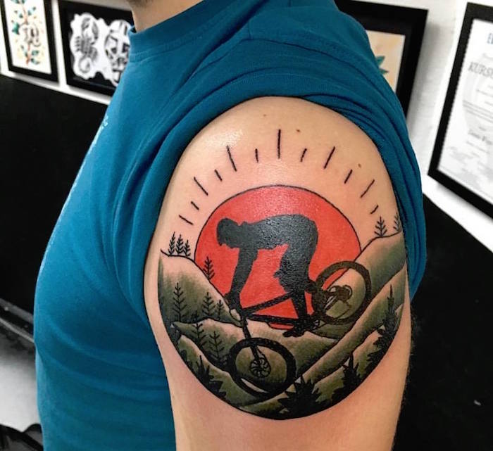 tatouage homme épaule cycliste vélo montagne soleil couchant rouge sur haut du bras