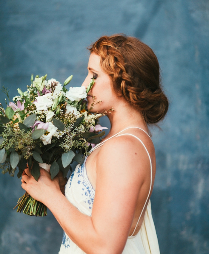 coiffure chignon tresse avec une tresse de côté sur cheveux longs roux, robe de mariée blanches à motifs bleus