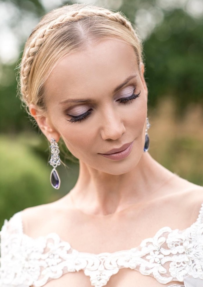 tresse-en-couronne-autour-de-la-tete-chveux-blond-raides-maquillage-de-mariée-violet-glamour couronne tresse autour du visage, cheveux blond, boucles d oreilles violettes, robe de mariée dentelle