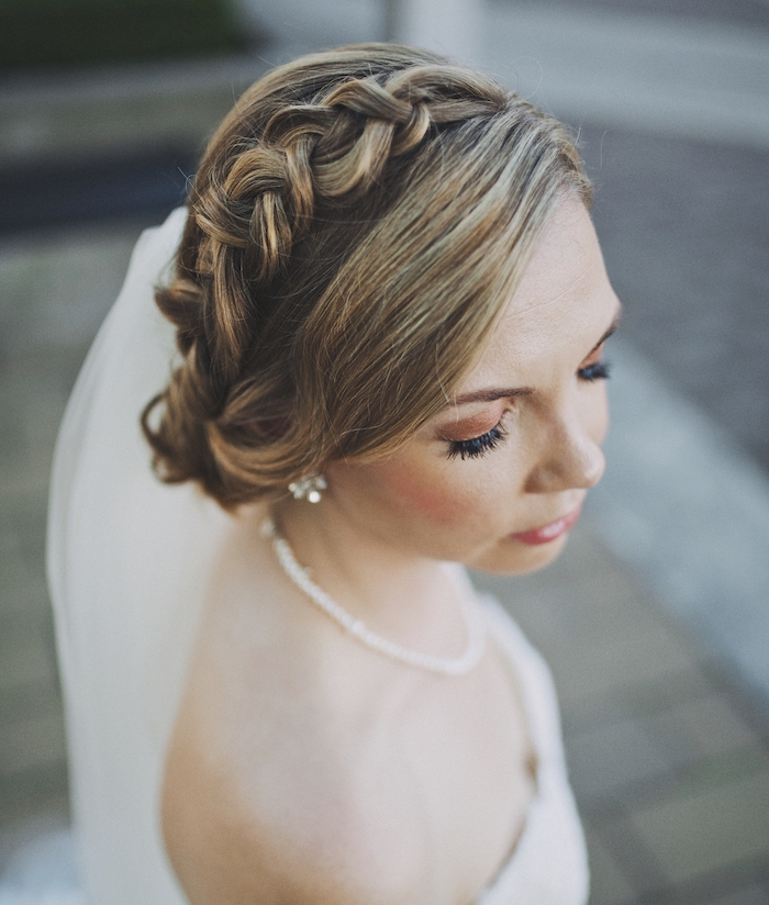 une-simple-tresse-volumineuse-dans-cheveux-ramassés-en-arrière-en-chignon-bas-mariage chignon tressé mariage avec une tresse autour de la tete couronne et meche de coté, collier d eperles blanches