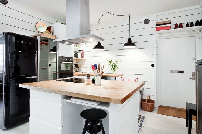 cuisine blanche et bois aménagée dans un style vintage scandinave aux accents noirs équipée d'un ilot de cuisine de cuisson avec coin bar intégré