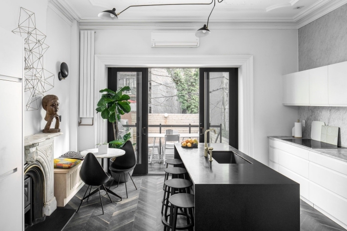 une petite cuisine blanche aménagée en longueur qui partage l'espace avec le salon design, séparée par l'espace séjour par un ilot de cuisine noir mat 