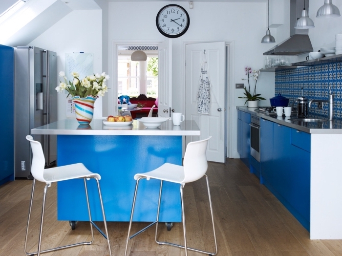 aménagement fonctionnel d'une petite cuisine avec ilot central à roulettes aux mêmes couleurs blanc et bleu que les armoires et la crédence