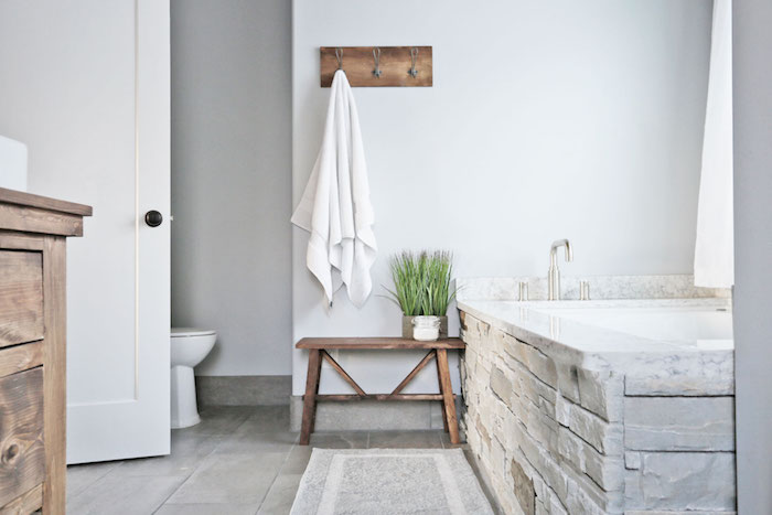 baignoire en pierre encastrée, sol en dalles carreaux de ciment, banc en bois, murs blancs, meuble lavabo bois brut