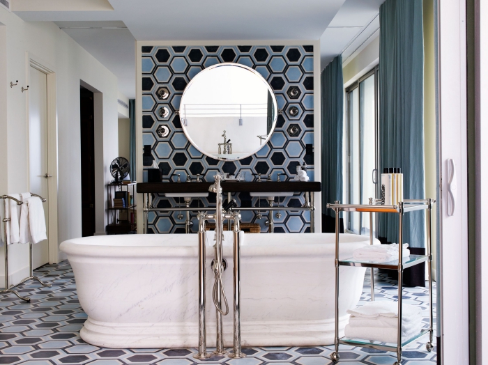 une baignoire îlot tendance au coeur de cette salle de bains de forte personnalité recouverte de carreaux de ciment à motifs hexagonaux noir et bleu 