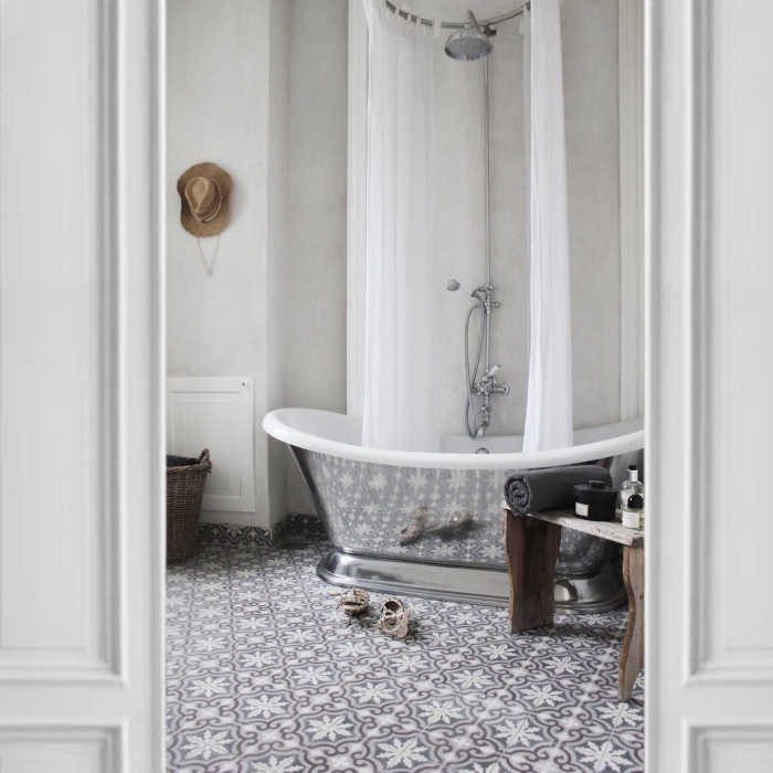 le revêtement de sol en carrelage carreaux de ciment à motifs arabesques délicats et l'aspect chromé de la baignoire créent une ambiance chic dans cette salle de bains monochrome
