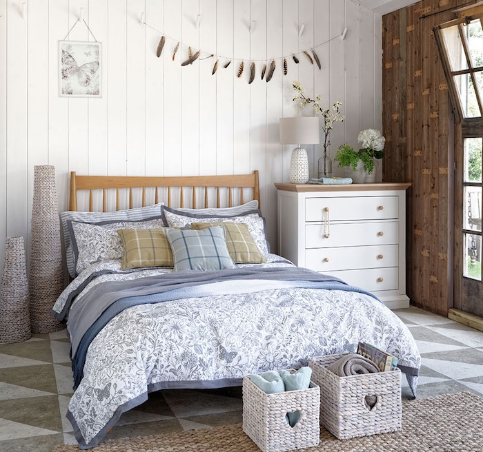 lambris blanchi, lit en bois, linge de lit blanc et bleu, tapis à grosses mailles, commode blanc, paniers de rangement bout de lit, deco murale plumes, deco de charme