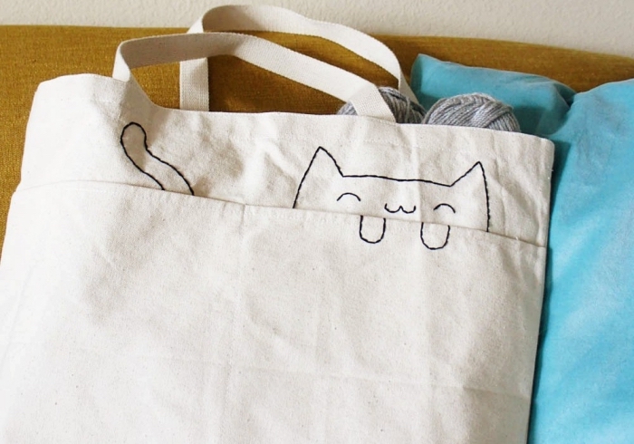 petite déco sur un tote bag blanc avec fil noir, idée broderie facile aux motifs visage et queue de chat sur un sac à main