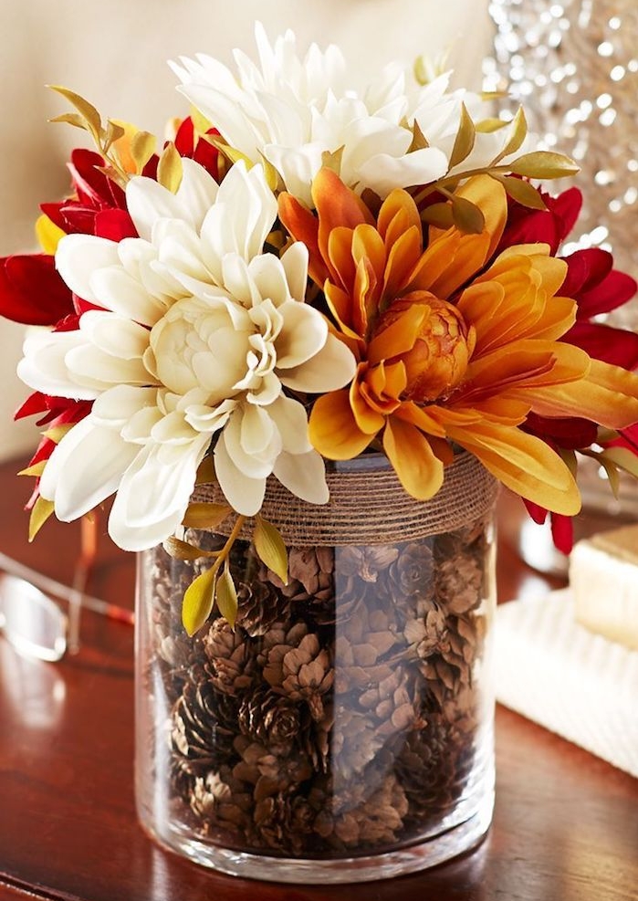 centre de table automne en vase de verre rempli de pommes de pin et décoré de ficelle, fleurs d automne