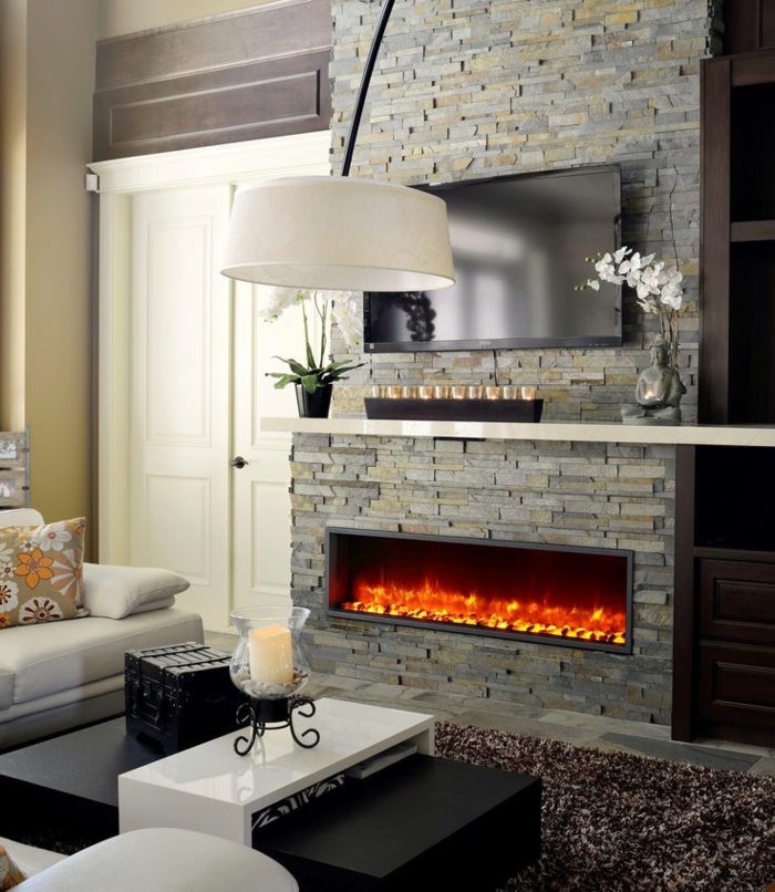 cheminée à effet flammes, manteau en briques grises, bougeoir décoratif sur une table basse blanche, 