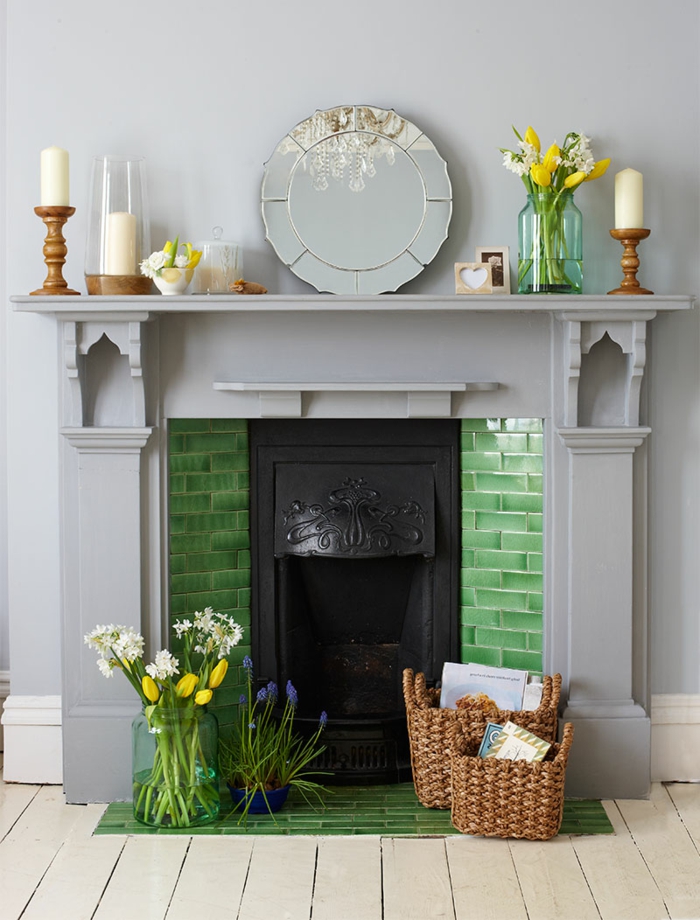 cheminée murale couleur gris clair, briques vertes, petit miroir rond, vases avec fleurs, paniers décoratifs