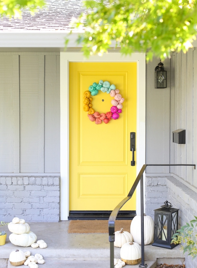 idee deco de porte en jaune avec une couronne de mini citrouilles colorées et des citrouilles de tailles variées sur les escaliers