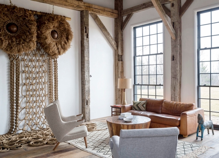 salon à design rustique avec meubles de bois et cuir aux murs blancs avec colonnes en bois brut, modèle suspension murale macramé