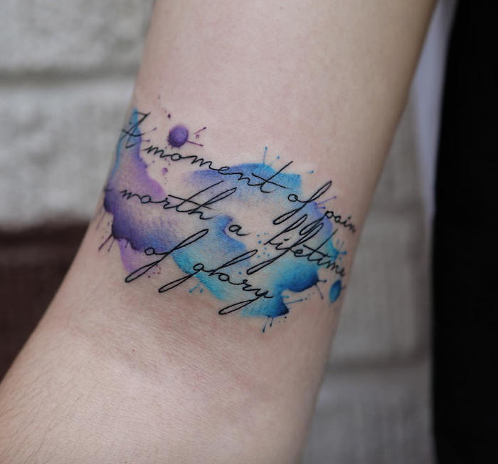 tatouage citation manuscrite noire sur fond de taches aquarelle couleurs sur bras