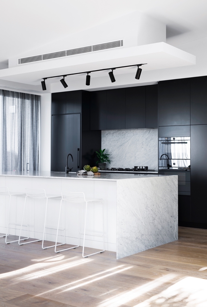 contraste saisissant entre les armoires de cuisine à finition noire mate et le plan de travail ilot central en marbre veiné accessoirisé avec des tabourets de bar en fil de métal blanc