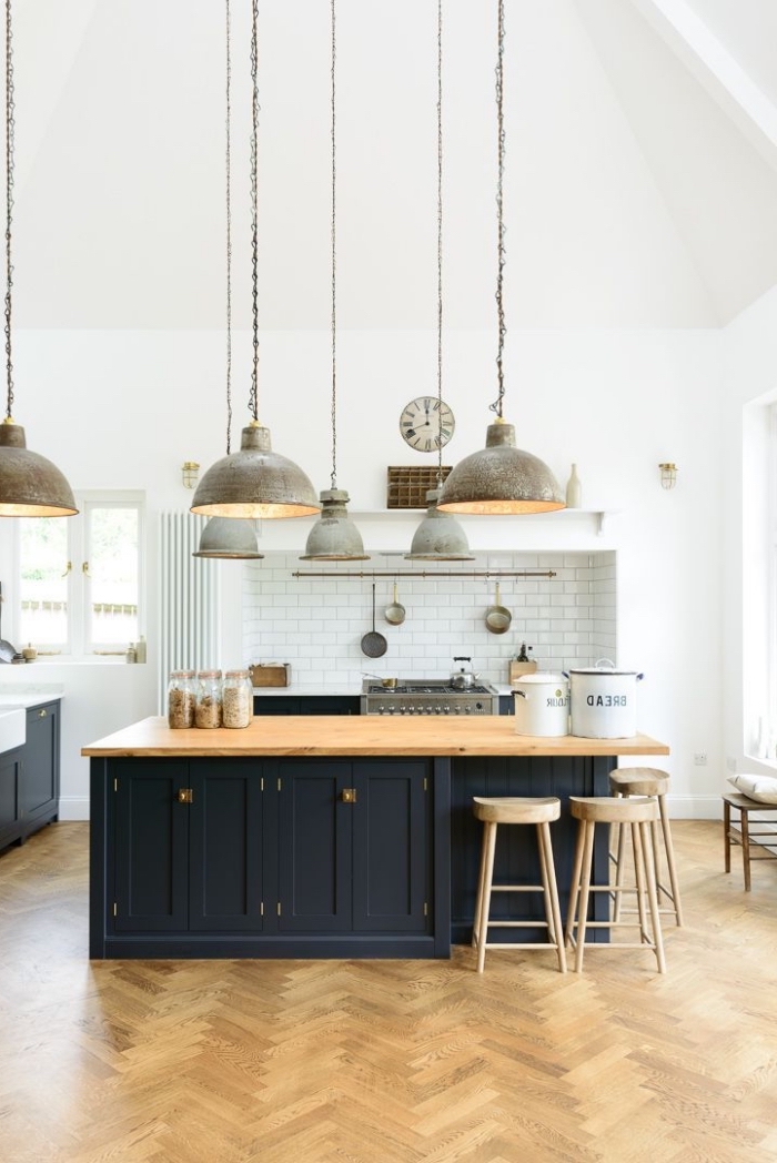 une grande cuisine aménagée en style atelier avec un ilot central cuisine deux couleurs surmonté des luminaires suspendus industrielles