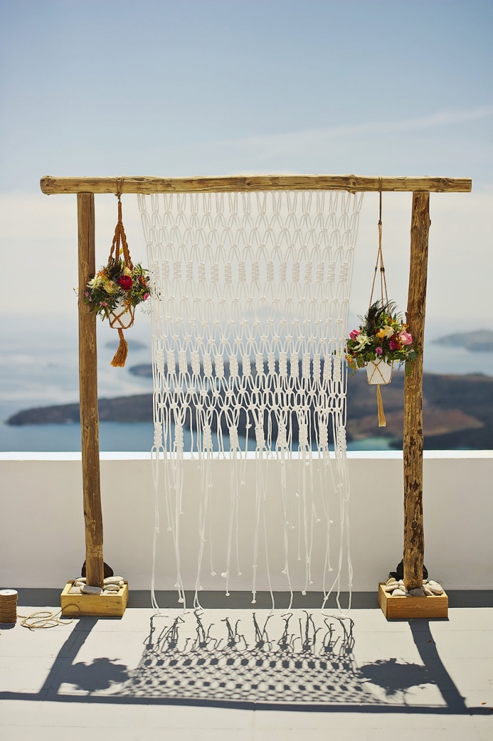 exemple de décor mariage en style boho avec un arc en bois et rideaux en macramé, modèle de suspension plante en fil rouge