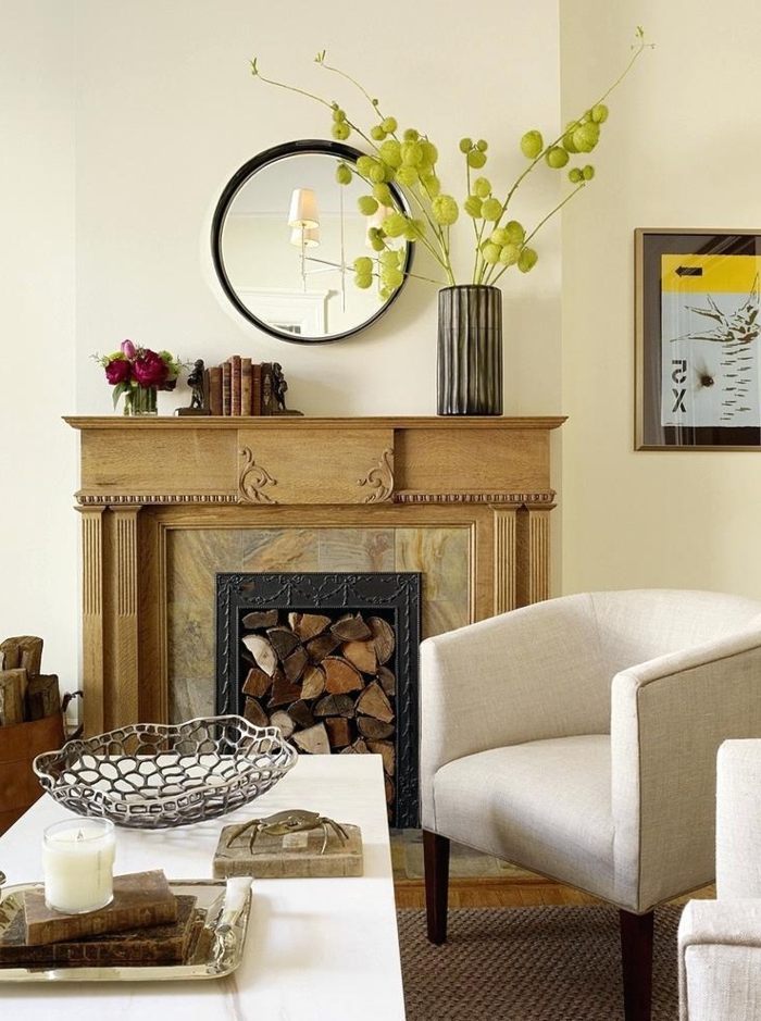miroir rond décoratif, cheminée murale en bois, fauteuils blancs, vase avec plante verte