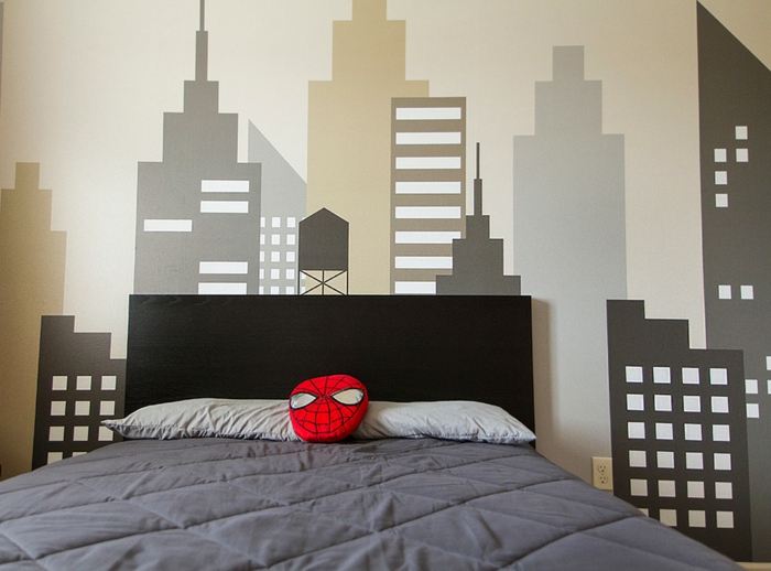 coussin en forme de masque de spiderman, dessins muraux gratte-ciel, grand lit dans une chambre gris et blanc