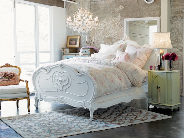 mur défraichi, lit vintage chic blanc, parure de lit motifs fleuris, tapis floral, sol gris foncé, chaise vintage, lustre élégant