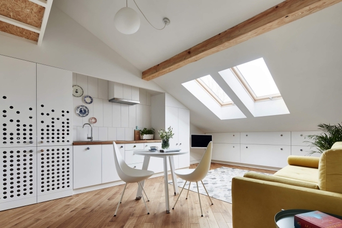 modèle de cuisine blanche ouverte aménagée avec meubles en bois et blanc, exemple comment décorer une pièce mansardée avec poutres en bois massif
