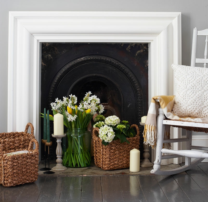 fleurs blanches en paniers rustiques, bougies blanches, chaise bercante près de la cheminée 