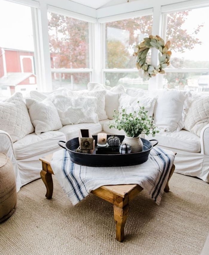 deco campagne dans un salon chaleureux avec canapé d angle blanc, table basse bois brut, centre de table fleurs, bougies et objets anciens