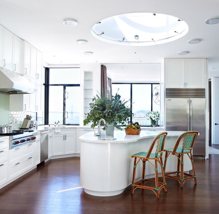 cuisine blanche moderne avec des électroménagers en acier inoxydable et un ilot centrale ergonomique d'une forme arrondie 