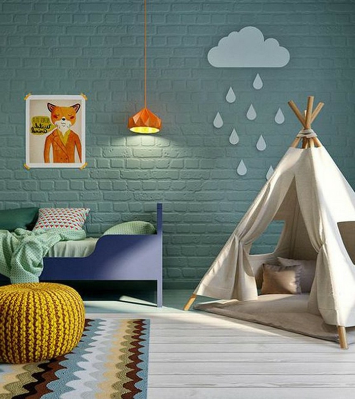 mur en briques vertes, tipi enfant, tabouret jaune tricoté, lit enfant bleu, dessin encadré et lampe orange