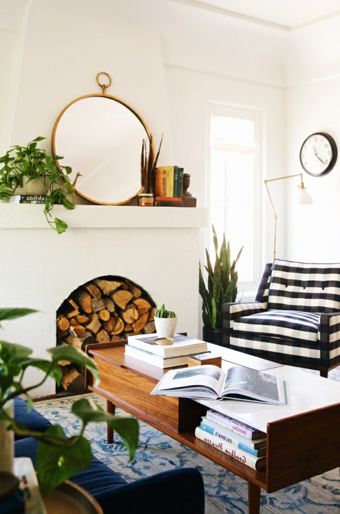 miroir rond et plantes vertes autour d'une cheminée blanche décorative, fauteuil rayé, tapis floral