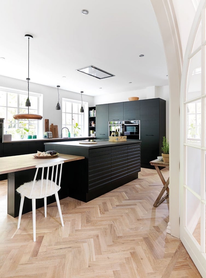 ambiance scandinave épurée dans cette cuisine aux armoires à finition noir mat qui s'organise autour de l'ilot central avec table en bois intégrée
