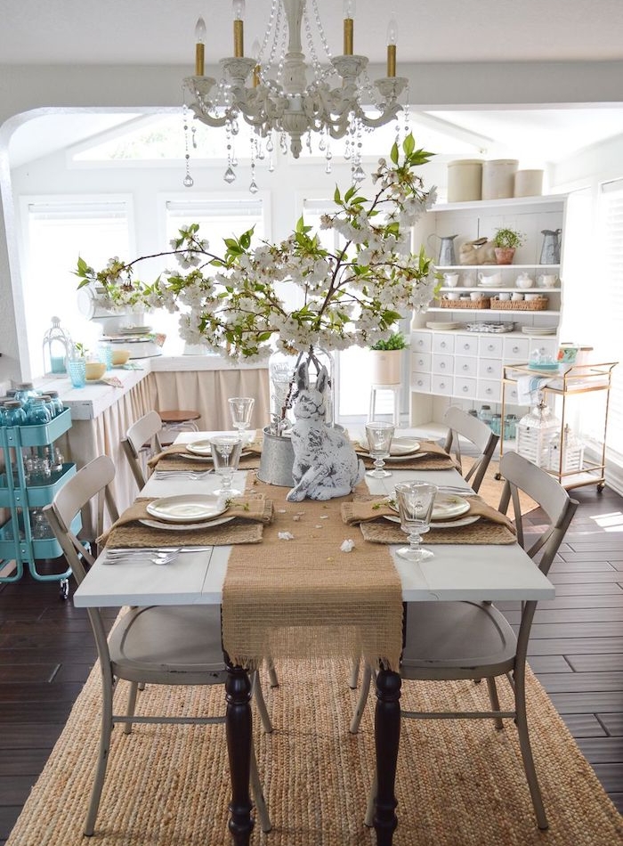 vaisselier blanc vintage, table en bois avec plateau blanc et chaises en bois usés, tapis beige, lustre élégant, sol parquet marron, deco maison de campagne