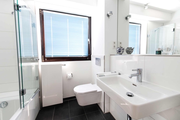 aménagement de petite salle de bain blanche avec large miroir, équipement salle de bain avec baignoire douche et cuvette wc suspendue