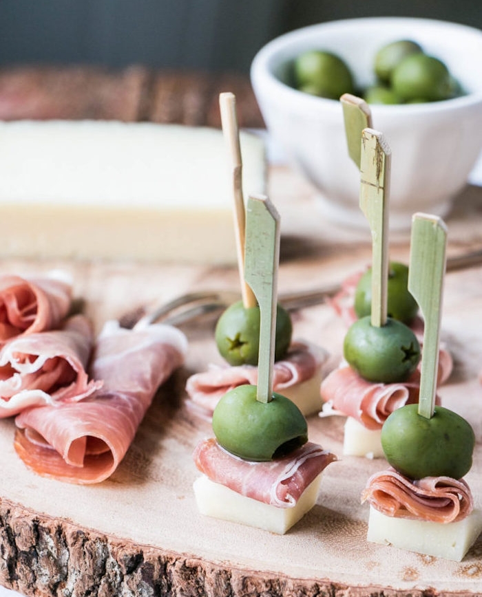 idée de brochette apero simple en fromage manchego, olive et prosciutto servi sur un rondin en bois, repas entre amis