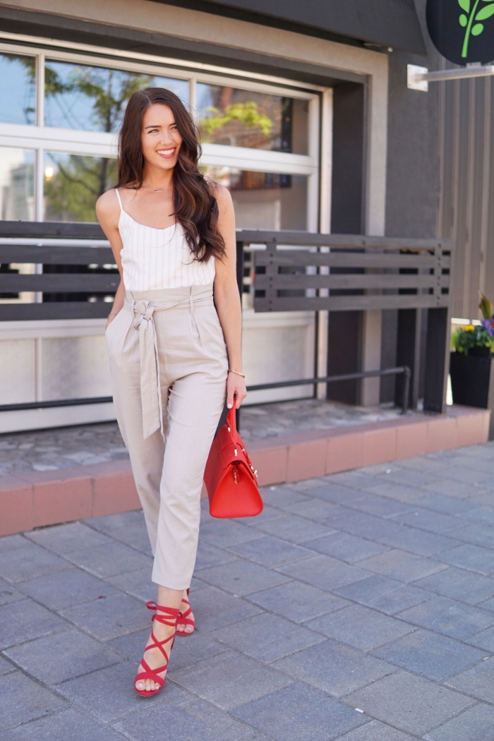 femme bien habillée en combinaison casual chic avec pantalon slim en beige et top rayé en blanc accessoirisé avec sandales et sac à main rouge