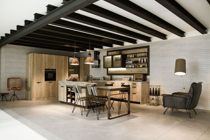 poutres noires au plafond, sol gris, ilot de cuisine avec rallonge table à manger, briques blanches