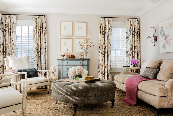 exemple de decoration campagne salon avec tapis beige, canapé marron clair, table basse ronde grise, chaises blanches, rideaux fleuris, commode ancienne bleue