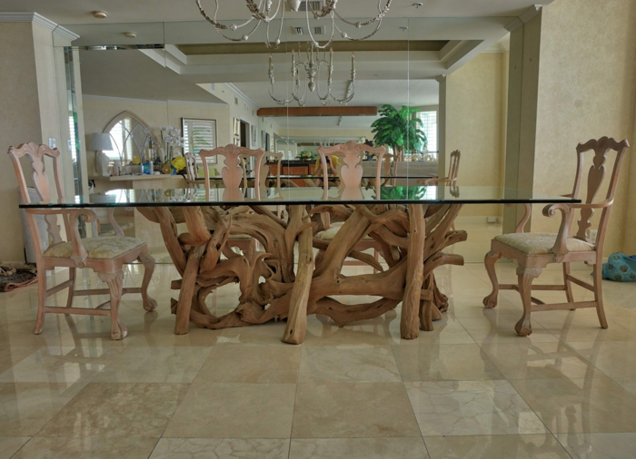 table de repas de bois flotté et verre, chaises en bois clair, sol en dalles beiges, chandelier