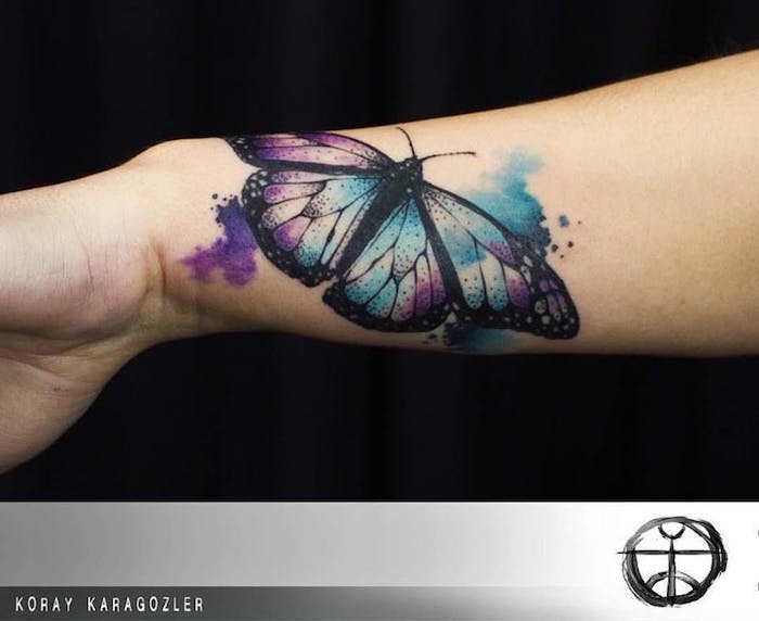 tattoo papillon noir sur taches aquarelle couleurs bleu turquoise et violet sur poignet et avant bras par koray karagozler