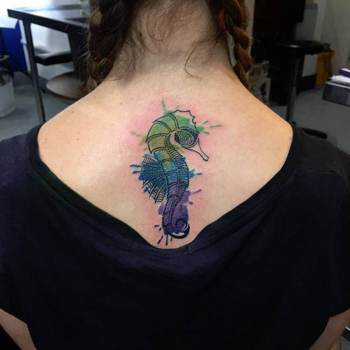 tatouage hippocampe noir et taches aquarelle vert bleu violet sur dos femme 