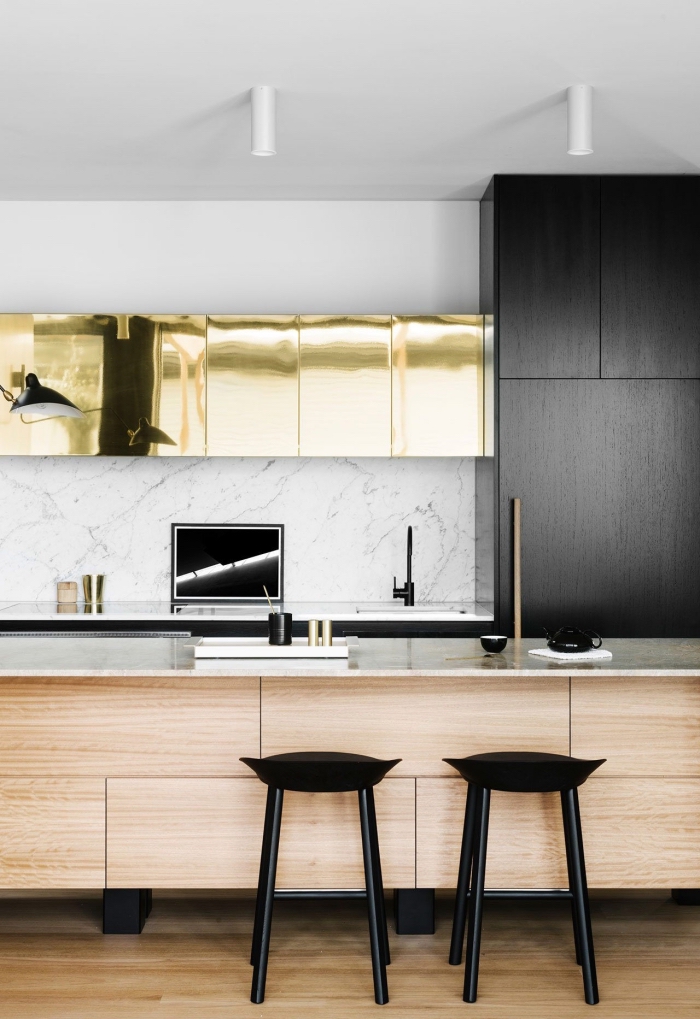 des effets de matières dans cette cuisine ilot central avec espace bar pour un look contemporain plein de caractères, des armoires de cuisine noir mat, or et bois 