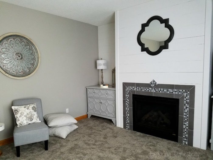manteau cheminée en carrelage gris et mosaique style credence sur mur en bois blanc dans salon avec moquette taupe et plat arabe en métal sur le mur gris