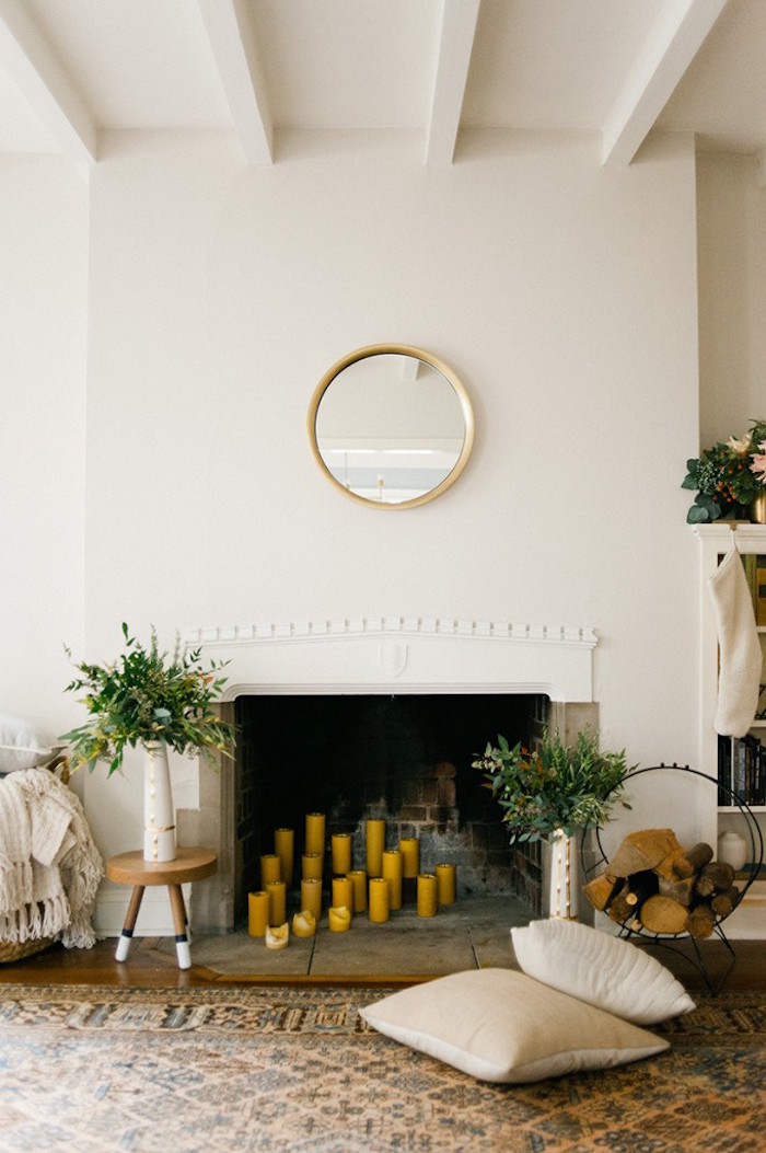 cheminée encastrée dans mur blanc avec manteau sculpté minimaliste avec bougies jaunes dans foyer et miroir circulaire or vintage